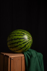 View of a whole watermelon on a green cloth with a black background, vertically, with copy space