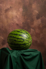 View of a whole watermelon on a green cloth with a dark background, vertically, with copy space