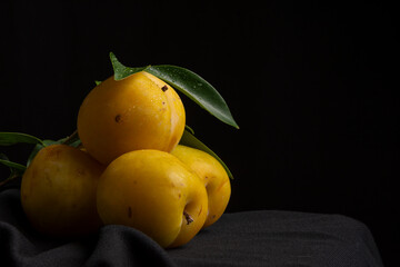 Close-up of yellow plums with green leaves, on a cloth and black background, horizontally with copy space