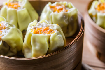close up of dim sum in a bamboo basket with chopsticks, on a wooden table