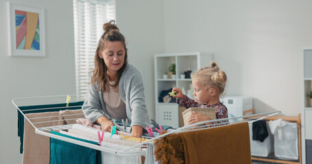 A mother hangs freshly washed clothes on the dryer in the bathroom while her daughter helps by...