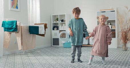 Siblings spend time together in the laundry room, standing near a washing machine, holding hands...