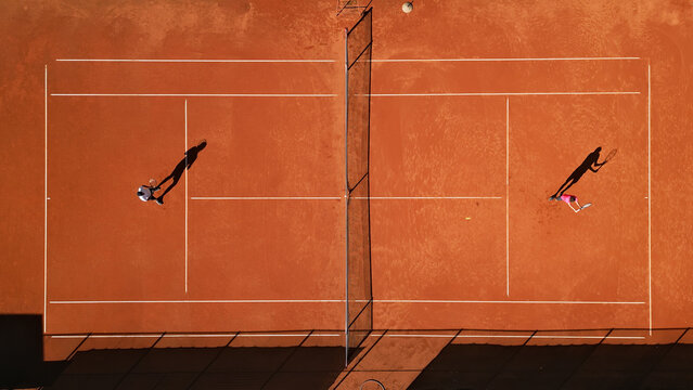 Drone shot of two athletes practicing on a clay tennis court, highlighting dynamic movement and focus. Captures intense training, skill development, and competitive spirit.