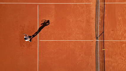 Tennis player practices on clay court, showcasing focused training. Aerial drone shot highlights stance, shadow, dedication, and skill development in a professional sports setting. © wkproduction