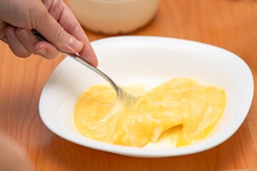Mixing egg yolk and white with a metal fork in a white ceramic plate for cooking