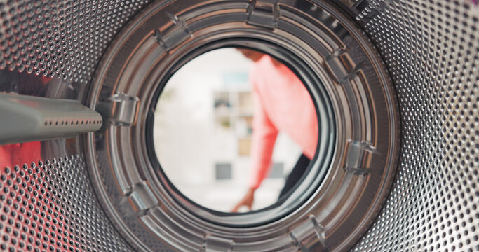 From the washing machine perspective, a mature woman carefully packs laundry into the drum, sorting vibrant fabrics, beginning the washing routine at home.