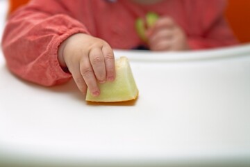 A small child's hand holding a piece of ripe melon for weaning and transition to solid foods