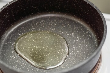 A puddle of olive oil heating in a small round pan for healthy cooking preparation