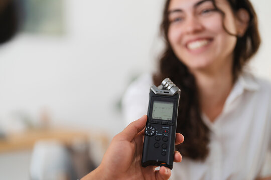 A person holds a digital audio recorder to interview a smiling woman, capturing sound for a podcast or project.