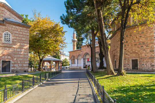 Exterior view of Hamza Bey Mosque in Bursa with its distinctive brickwork, Turkish flag, and surrounding trees.