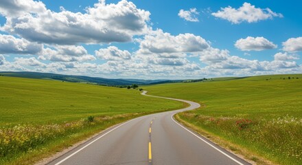 Fototapeta premium Winding road through green fields under cloudy blue sky suggesting travel and exploration