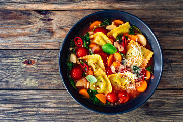 Italian ravioli soup with vegetables on wooden table