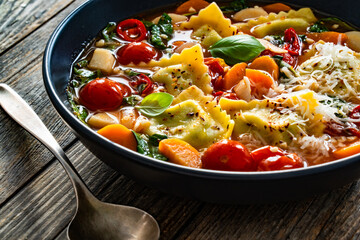 Italian ravioli soup with vegetables on wooden table