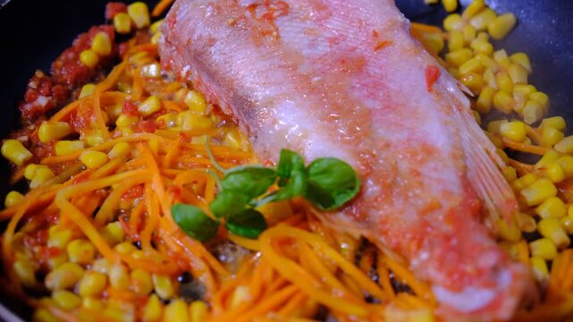 Fresh Red Snapper hot in the frying pan with carrot, garlic, basil, corn, savoury sauce, vegetables garnish. Brazil food