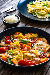 Italian ravioli soup with vegetables on wooden table