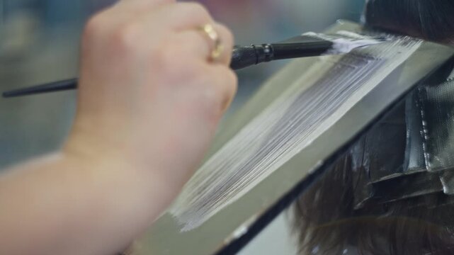Hairdresser applying bleach and hair dye close up in professional salon showing coloring process hairstyle transformation and beauty care treatment for women