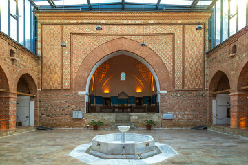 Ottoman courtyard of Muradiye Madrasa in Bursa with marble fountain, arched entrance and brick wall decorations.