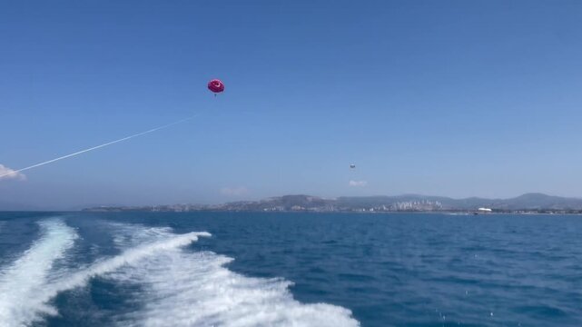 People flying on parachute in blue sky. Parasailing in Turkey, Kusadasi, Audin coast. Real time 4k video footage.