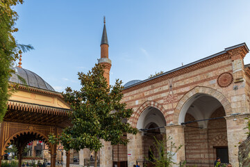 Historic Orhan Mosque in Bursa with Ottoman brick and stone architecture, arches and tall minaret.