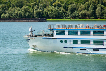 The bow of a large passenger river cruise ship sailing calmly on the river's surface on a clear day