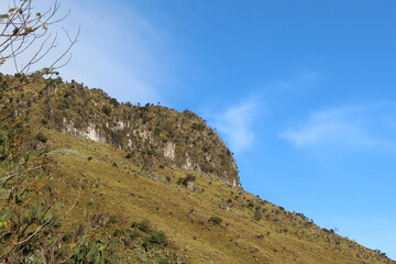 Striking landscape photograph featuring a rugged mountain slope covered in green grass and scattered shrubs