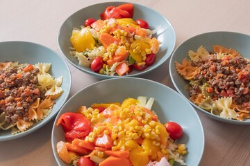Variety of homemade meals. Bowls with farfalle pasta and beef ragù, fresh corn salad with lettuce, peppers, tomatoes and ham. Healthy lifestyle, balanced diet and home cooking concept.
