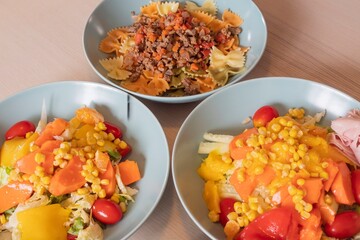 Variety of homemade meals. Bowls with farfalle pasta and beef ragù, fresh corn salad with lettuce, peppers, tomatoes and ham. Healthy lifestyle, balanced diet and home cooking concept.