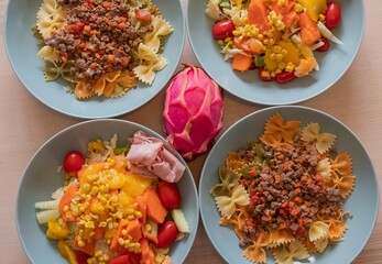 Variety of homemade meals. Bowls with farfalle pasta and beef ragù, fresh corn salad with lettuce, peppers, tomatoes and ham. Healthy lifestyle, balanced diet and home cooking concept.