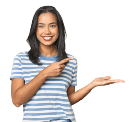 Young Latina posing in studio excited holding a copy space on palm.