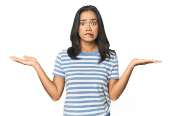 Young Latina posing in studio confused and doubtful shrugging shoulders to hold a copy space.