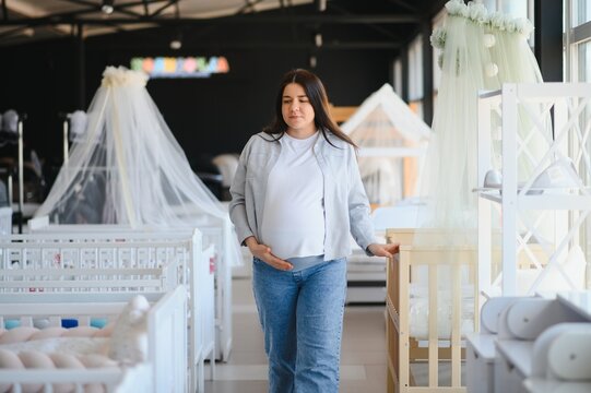 Smiling pregnant woman choosing baby crib at shopping mall - Powered by Adobe