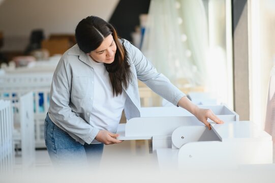 Pretty pregnant woman choosing changing table for newborn in infant shop