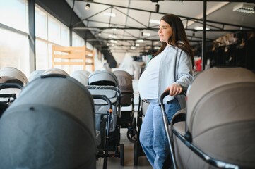 Pregnant woman choosing baby stroller at store. Mother doing shopping in baby shop