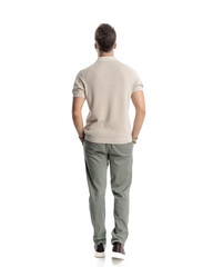 Fototapeta premium back view of young fashion man walking with hands in pockets