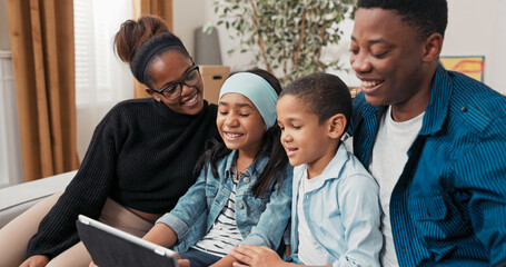In their new apartment, the family sits on the couch video chatting with grandparents. Parents and children smile and wave at the tablet, sharing joy from their new place.