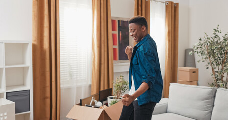 Man full of energy and optimism is dancing in middle of living room in a new apartment, the guy is happy to move around him there are cardboard boxes with packed things joy smiles new chapter of life