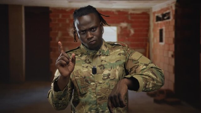 Man in camouflage uniform with dog tags points finger up and points down inside building; determination duty discipline.