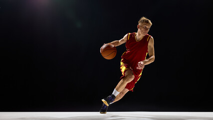 Basketball player dribbling with focus and energy on dark background. Concept of competition, fitness branding, advertising, social media design, and motivational sports imagery.