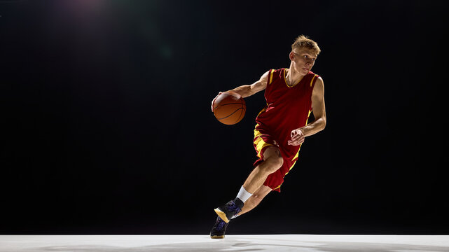 Basketball player dribbling with focus and energy on dark background. Concept of competition, fitness branding, advertising, social media design, and motivational sports imagery.