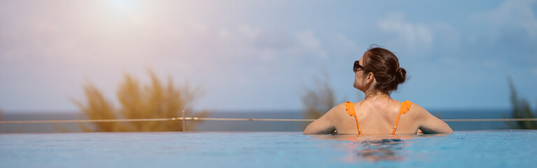 Tourist relaxing in infinity pool enjoying ocean view