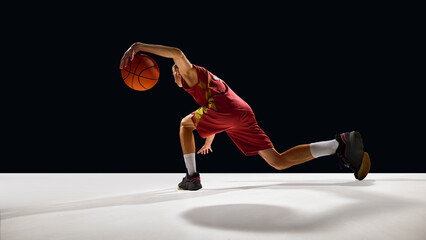 Basketball player stretching low dribble move on court with emotional energy. Concept of athletic intensity, branding design, sport lifestyle, and fitness motivation campaigns.