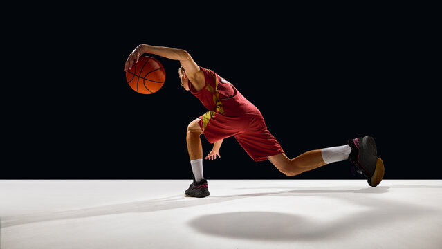 Basketball player stretching low dribble move on court with emotional energy. Concept of athletic intensity, branding design, sport lifestyle, and fitness motivation campaigns. - Powered by Adobe