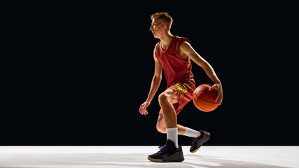 Focused basketball player dribbling ball on court in red uniform with strength. Concept of sport lifestyle, fitness passion, branding visuals, and emotional competitive action.