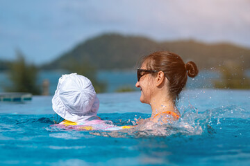 Mother and daughter enjoying swimming pool on sunny summer day