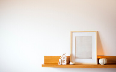 Minimalist shelf display featuring a blank picture frame, decorative ceramic house, and a candle, creating a serene and stylish home decor atmosphere with copy space