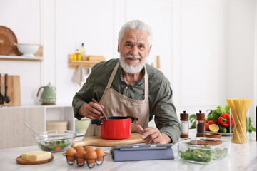Elderly man using tablet while cooking at white marble table in kitchen