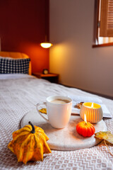 Cozy autumn scene featuring a warm cup of coffee, decorative pumpkins, and a candle on a marble tray, creating a relaxing atmosphere in a stylish bedroom
