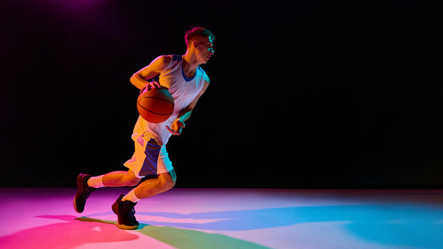 Basketball player moving with ball under neon lights full of energy. Concept of branding, digital campaigns, motivational visuals, lifestyle advertising, and athletic inspiration.
