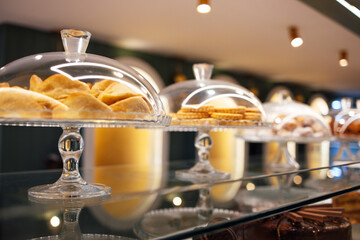 Display of assorted baked goods under glass domes in a modern bakery, showcasing delicious pastries and cookies on a stylish countertop with warm lighting
