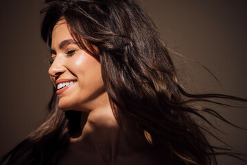 Smiling woman with long, flowing hair illuminated by soft light, showcasing natural beauty and joy in a serene atmosphere, embodying happiness and confidence